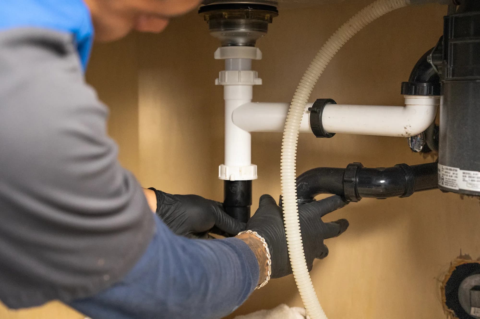 Plumber in black gloves working on the drain lines under a Phoenix kitchen sink